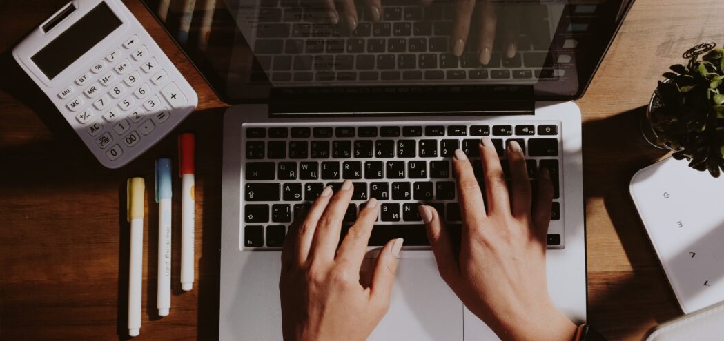 Laptop mit Taschenrechner, Pflanze und drei Stifte grün, blau, rot